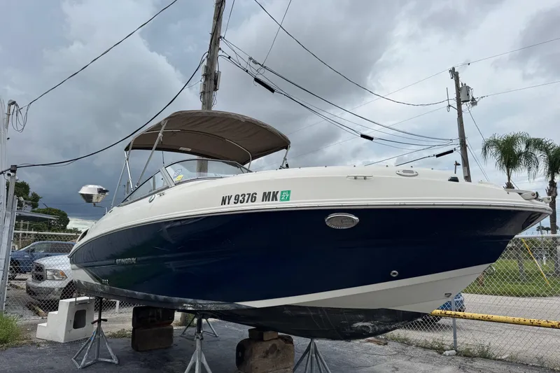 Slide: The Image of 2015 Stingray 215 LR boat on stands, overcast sky, fenced area. - 2