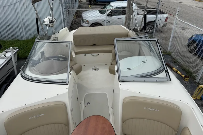 Slide: The Image of 2015 Stingray 215 LR boat interior with beige seating and windshield, parked in a lot. - 5