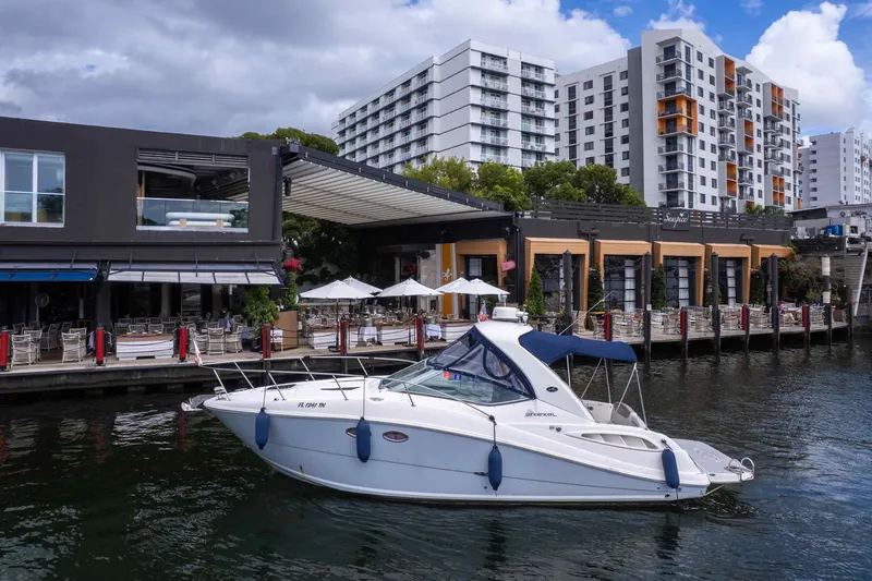 The Image of 2007 Sea Ray 290 Sundancer yacht docked near waterfront restaurant and modern buildings. - 0