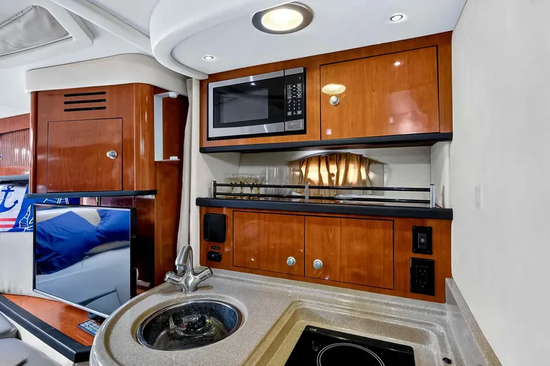 Slide: The Image of 2007 Sea Ray 290 Sundancer interior with kitchenette, featuring microwave, sink, and wooden cabinetry. - 35