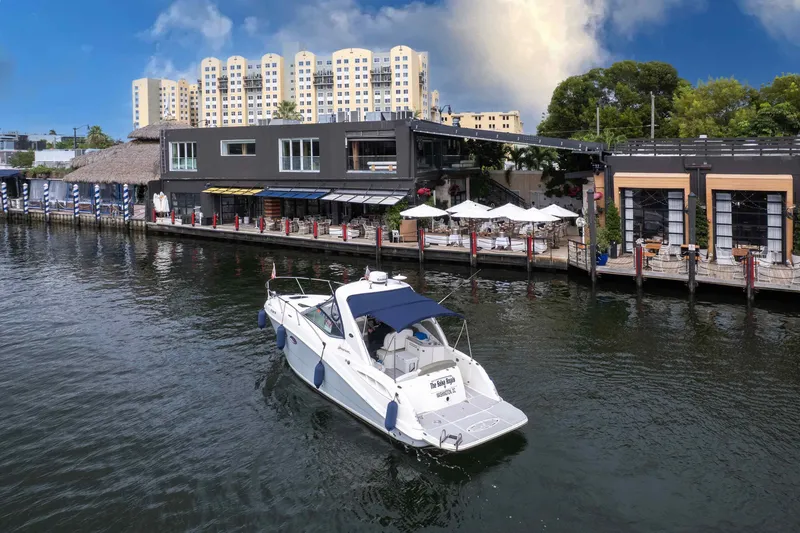 Slide: The Image of 2007 Sea Ray 290 Sundancer cruising near waterfront restaurant with modern buildings in background. - 6