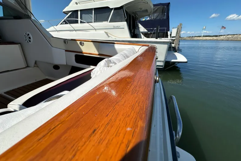 Slide: The Image of 1987 Sea Ray 340 Sundancer docked, showcasing polished wooden railing and serene marina view. - 9
