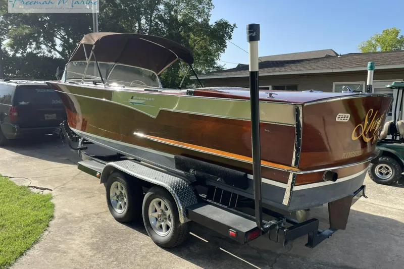 Slide: The Image of 1964 Shepherd 22 boat on trailer, parked in driveway, with brown and chrome finish. - 2