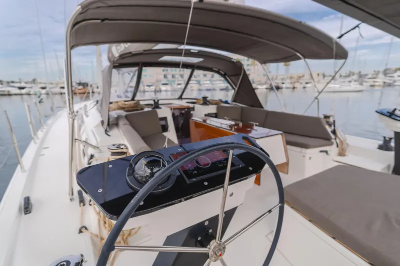 Slide: The Image of 2024 Dufour 470 yacht cockpit with steering wheel, spacious seating, and marina view. - 23