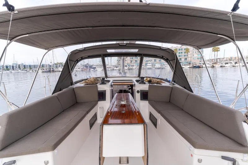 Slide: The Image of 2024 Dufour 470 yacht cockpit with cushioned seating and wooden table, docked in marina. - 25