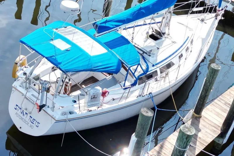 Slide: The Image of 1987 Catalina 34 sailboat docked, featuring blue canopy and white hull. - 4