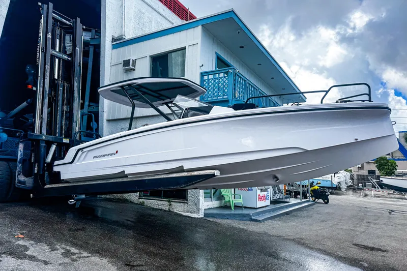 The Image of 2023 Axopar 25 Cross Top boat being lifted by a forklift near a building. - 0
