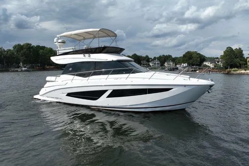 The Image of 2019 Regal 42 Fly yacht on calm water, under cloudy sky, near shoreline. - 1