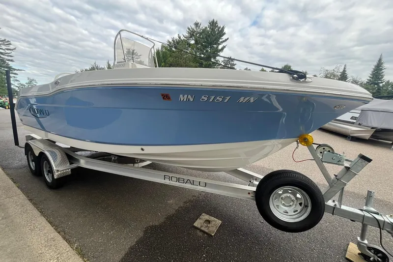 Slide: The Image of 2023 Robalo R200 Center Console boat on trailer, light blue hull, parked outdoors. - 21