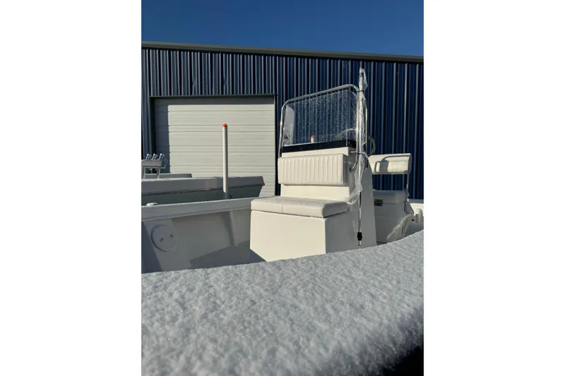 Slide: The Image of 2026 C-Hawk 18 Center Console boat with snow-covered deck, parked near a blue building. - 8