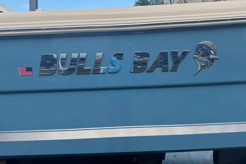 Slide: The Image of Bulls Bay 255 boat logo on blue hull, featuring American flag and fish emblem, 2026 model. - 7