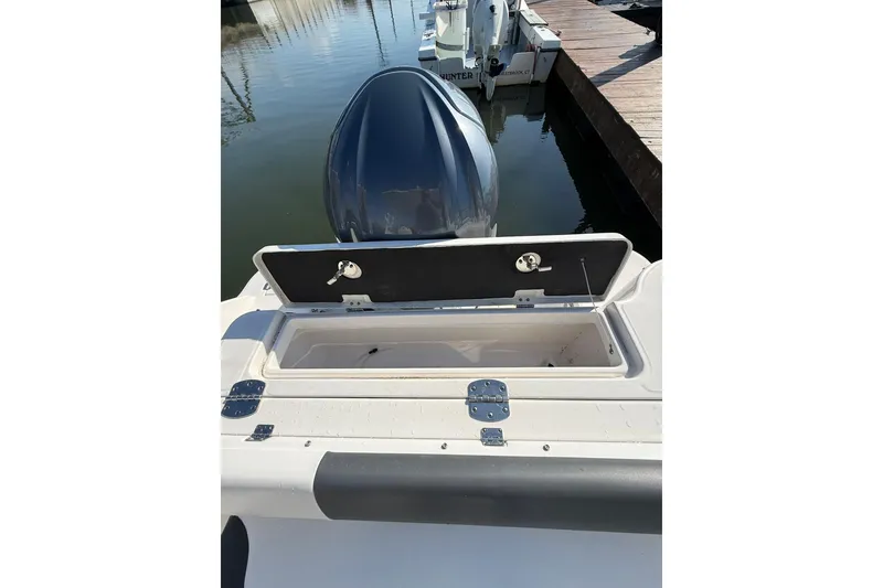 Slide: The Image of 2022 Robalo R247 Dual Console boat with open storage compartment, docked by the water. - 11