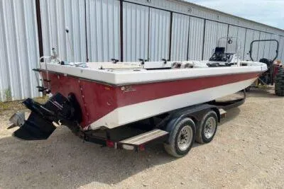 Slide: The Image of 2000 Falcon Striper boat on trailer, red and white, parked near a metal building. - 3
