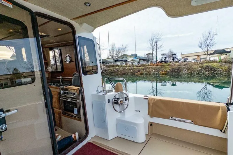 Slide: The Image of 2019 Ranger Tugs R-31-S boat interior with kitchen and helm, docked by calm water. - 7