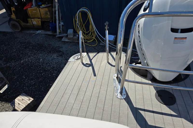 Slide: The Image of 2025 Godfrey Monaco 255 SB boat deck with railing and engine, docked on gravel. - 27