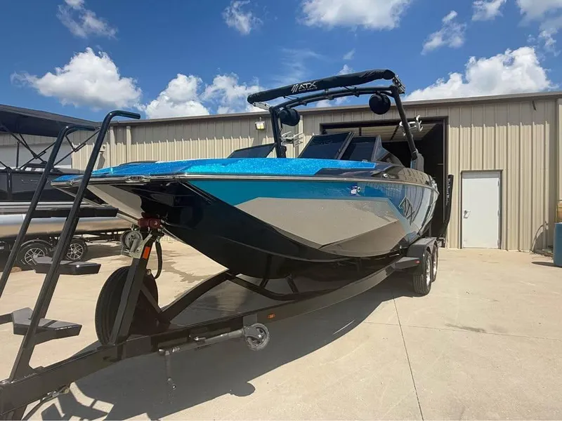 Slide: The Image of 2023 ATX Surf Boats 24 Type-S on trailer, parked outside a warehouse under a blue sky. - 2