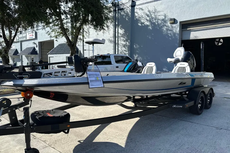 Slide: The Image of 2026 iKon LXE21 boat on trailer, parked outside a garage in daylight. - 2