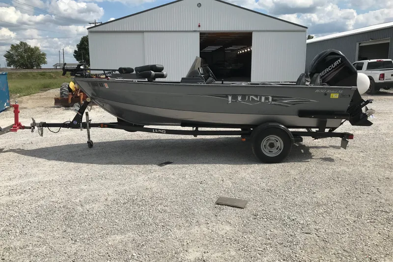Slide: The Image of 2014 Lund 1650 Rebel XL SS boat on trailer, parked outside a large garage. - 1