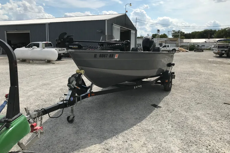 Slide: The Image of 2014 Lund 1650 Rebel XL SS boat on trailer in gravel lot, industrial background. - 5