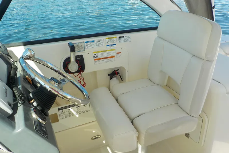Slide: The Image of 2013 Pursuit DC 265 Dual Console boat helm with steering wheel and white captain's seat. - 11
