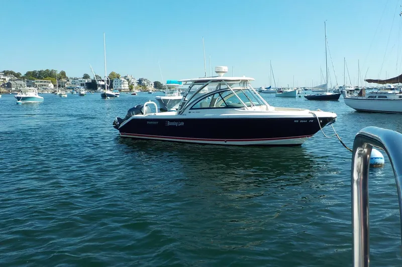 Slide: The Image of 2013 Pursuit DC 265 Dual Console boat anchored in a scenic harbor with other vessels. - 4