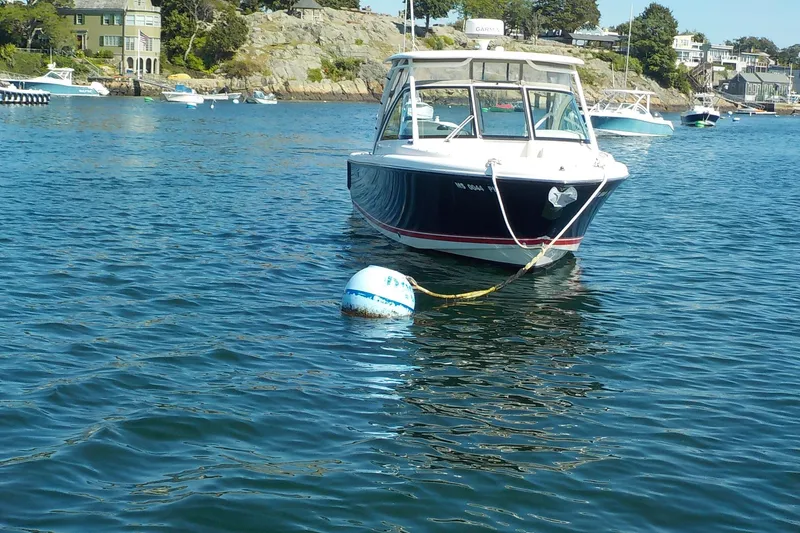Slide: The Image of 2013 Pursuit DC 265 Dual Console boat moored on calm water near rocky shoreline. - 5