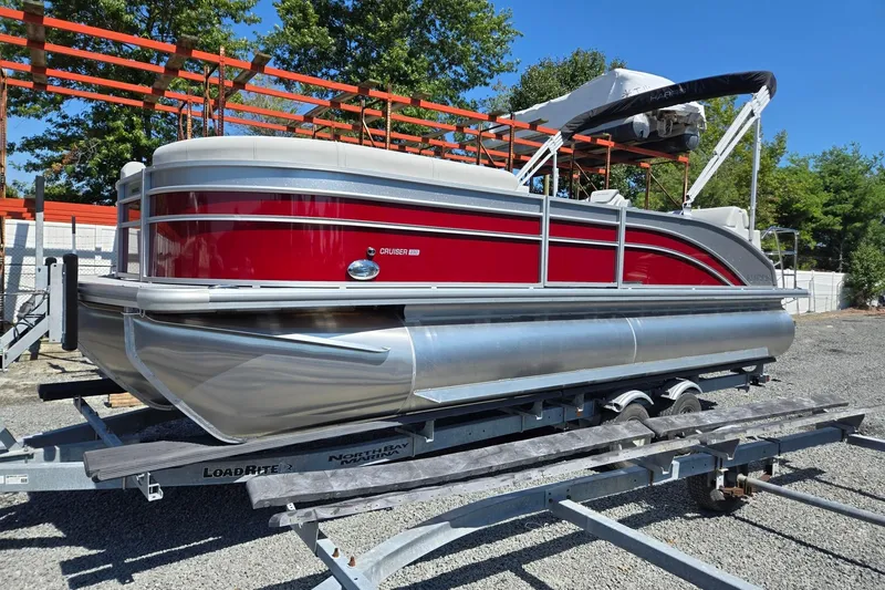 The Image of 2026 Harris Cruiser 230 pontoon boat with red and silver design on a trailer. - 0