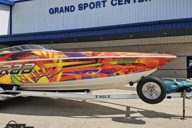 Slide: The Image of 1995 Wellcraft 29 Scarab boat with vibrant graphics on a trailer at Grand Sport Center. - 13