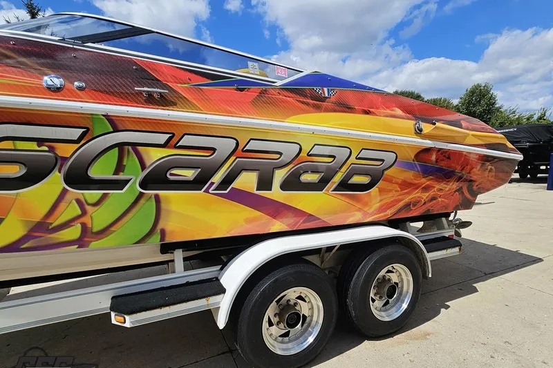 Slide: The Image of 1995 Wellcraft 29 Scarab boat with vibrant graphics on a trailer under a blue sky. - 25