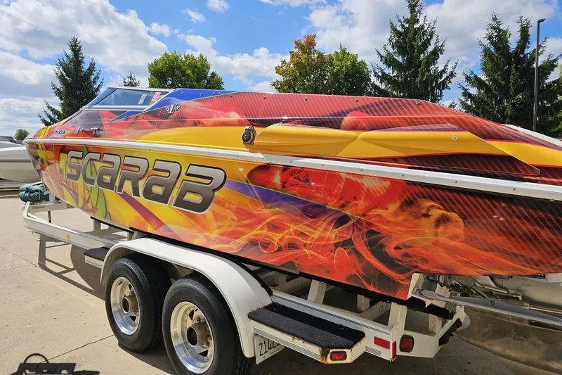 Slide: The Image of 1995 Wellcraft 29 Scarab boat with vibrant flame graphics on a trailer. - 27