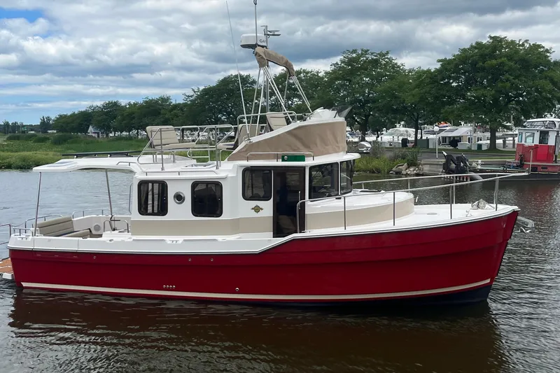 The Image of 2026 Ranger Tugs R-31 Command Bridge Luxury Edition, red hull, docked on a calm river. - 1