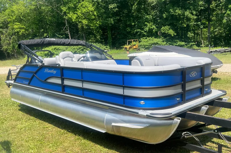 Slide: The Image of 2025 Bentley Pontoons Legacy QSB in vibrant blue, parked on grass with lush trees. - 7