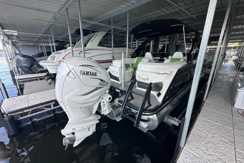 Slide: The Image of 2022 Bennington QX 25 Quad Bench interior with green and white seating, docked beside another boat. - 9