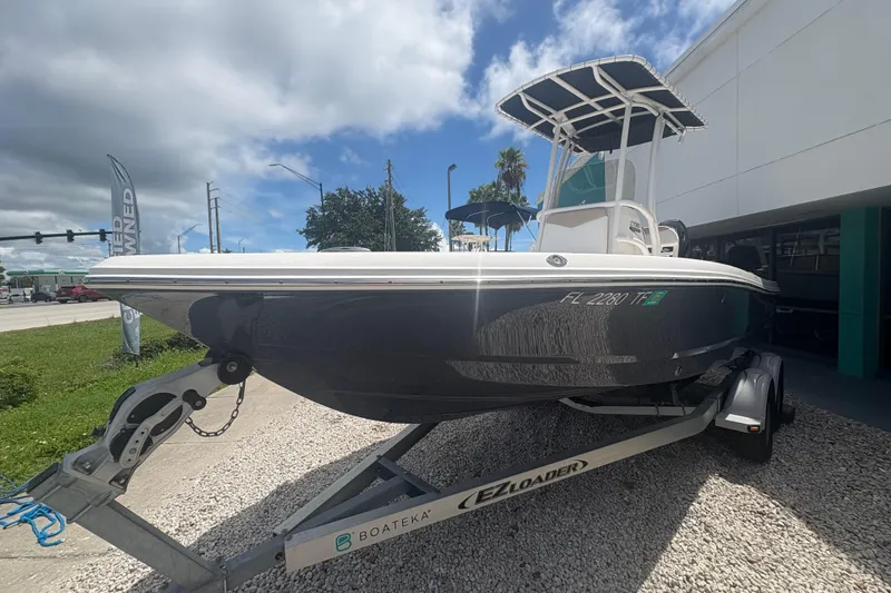 Slide: The Image of 2022 Robalo 206 Cayman boat on trailer, parked outdoors under a partly cloudy sky. - 2
