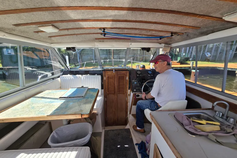 Slide: The Image of 1984 Bayliner 2802 Trophy boat interior with man at helm, featuring table and sink. - 17