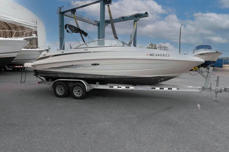 Slide: The Image of 2010 Sea Ray 240 Sundeck boat on trailer, parked outdoors under cloudy sky. - 2