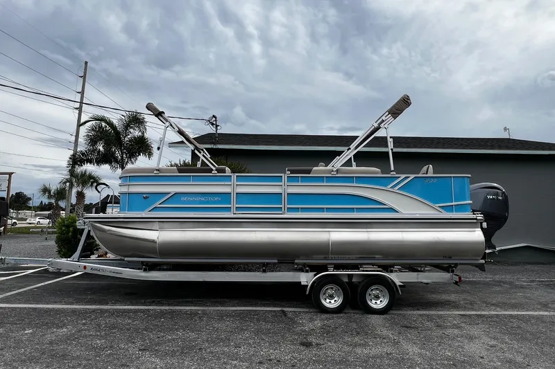 Slide: The Image of 2026 Bennington S22 pontoon boat on trailer, parked outdoors under cloudy sky. - 2