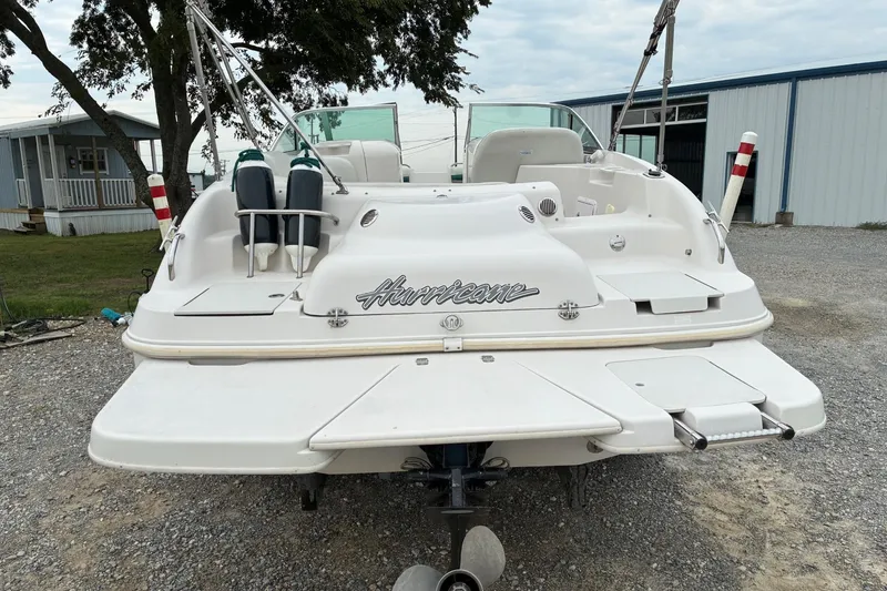 Slide: The Image of 2003 Hurricane 234 SD boat, rear view, parked on gravel near buildings and trees. - 3