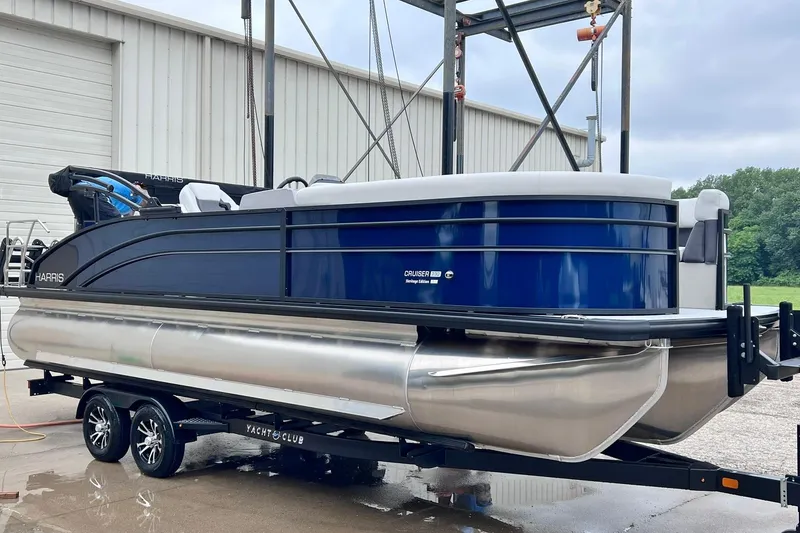 Slide: The Image of 2025 Harris Cruiser 230 Heritage Edition pontoon boat on trailer, blue and silver design. - 2