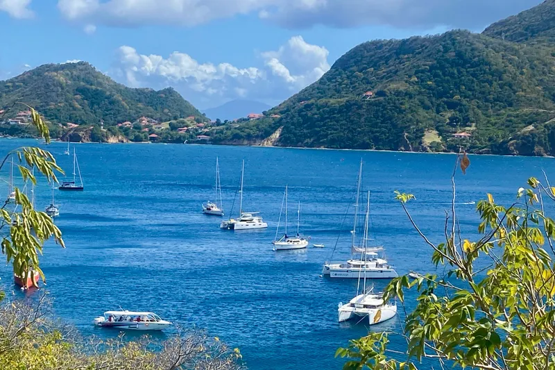 Slide: The Image of Sailboats anchored in a scenic bay surrounded by lush green hills. - 9