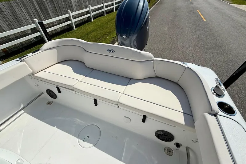 Slide: The Image of 2026 Sea Hunt Ultra 229 boat interior with cushioned seating and motor, parked on a road. - 7