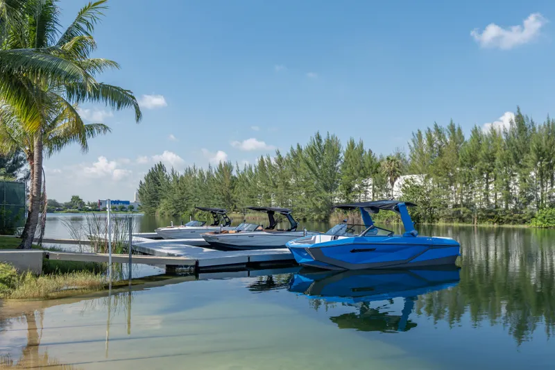 Slide: The Image of 2026 Nautique Super Air Nautique G23 boats docked on a serene lake with palm trees. - 40