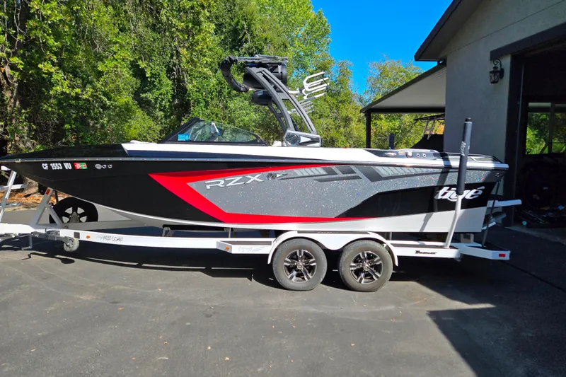 The Image of 2021 Tigé 22RZX boat on trailer, parked outdoors with lush greenery background. - 1