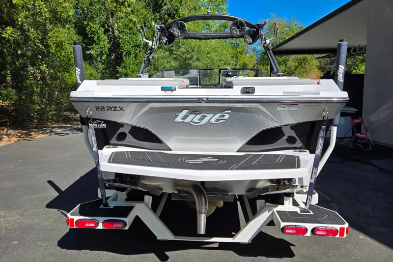 Slide: The Image of 2021 Tigé 22RZX boat, rear view, parked outdoors with lush greenery. - 3