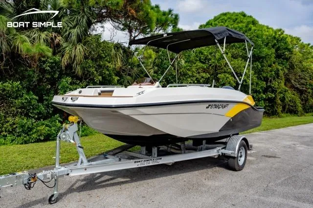 Slide: The Image of 2022 Starcraft SVX 191 OB boat on trailer, parked outdoors with lush greenery background. - 2