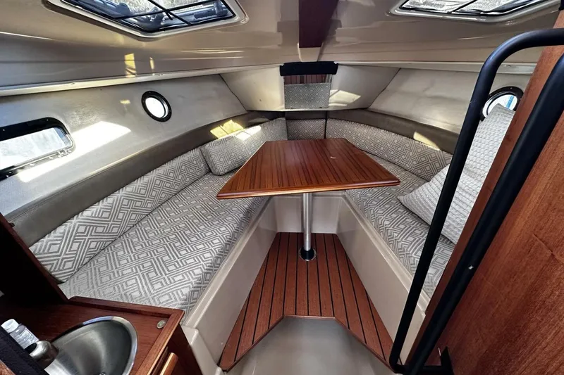 Slide: The Image of 2019 Ranger Tugs R-23 cabin interior with wood table, patterned cushions, and porthole windows. - 8