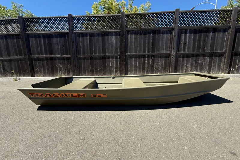 The Image of 2026 Tracker Grizzly 12 Jon boat on pavement, wooden fence background. - 0