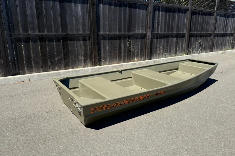 Slide: The Image of 2026 Tracker Grizzly 12 Jon boat on pavement, against a wooden fence background. - 3
