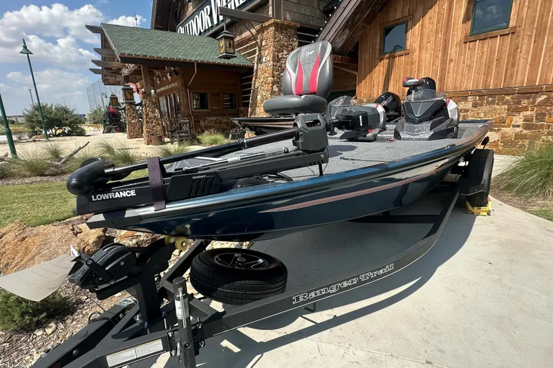 Slide: The Image of 2025 Ranger ALPHA 208 fishing boat on trailer, parked outside rustic building. - 1