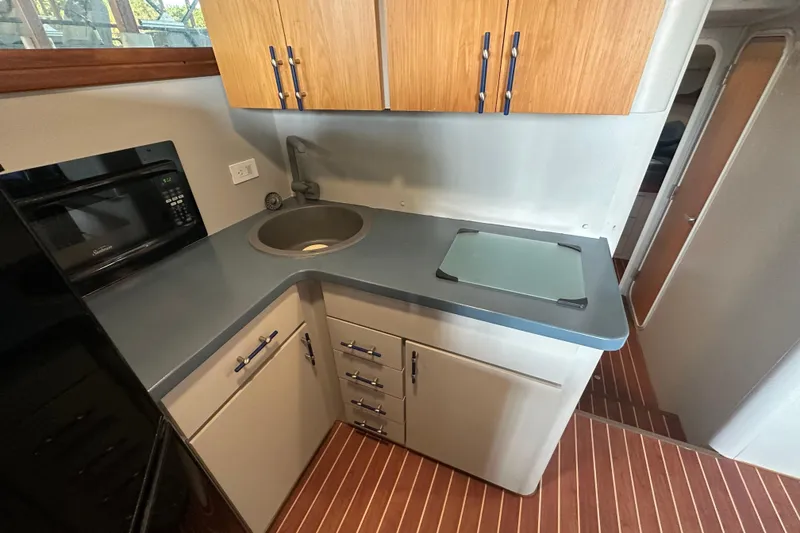 Slide: The Image of 1996 Mainship 40 Sedan Bridge kitchen with microwave, sink, and wooden cabinets. - 25